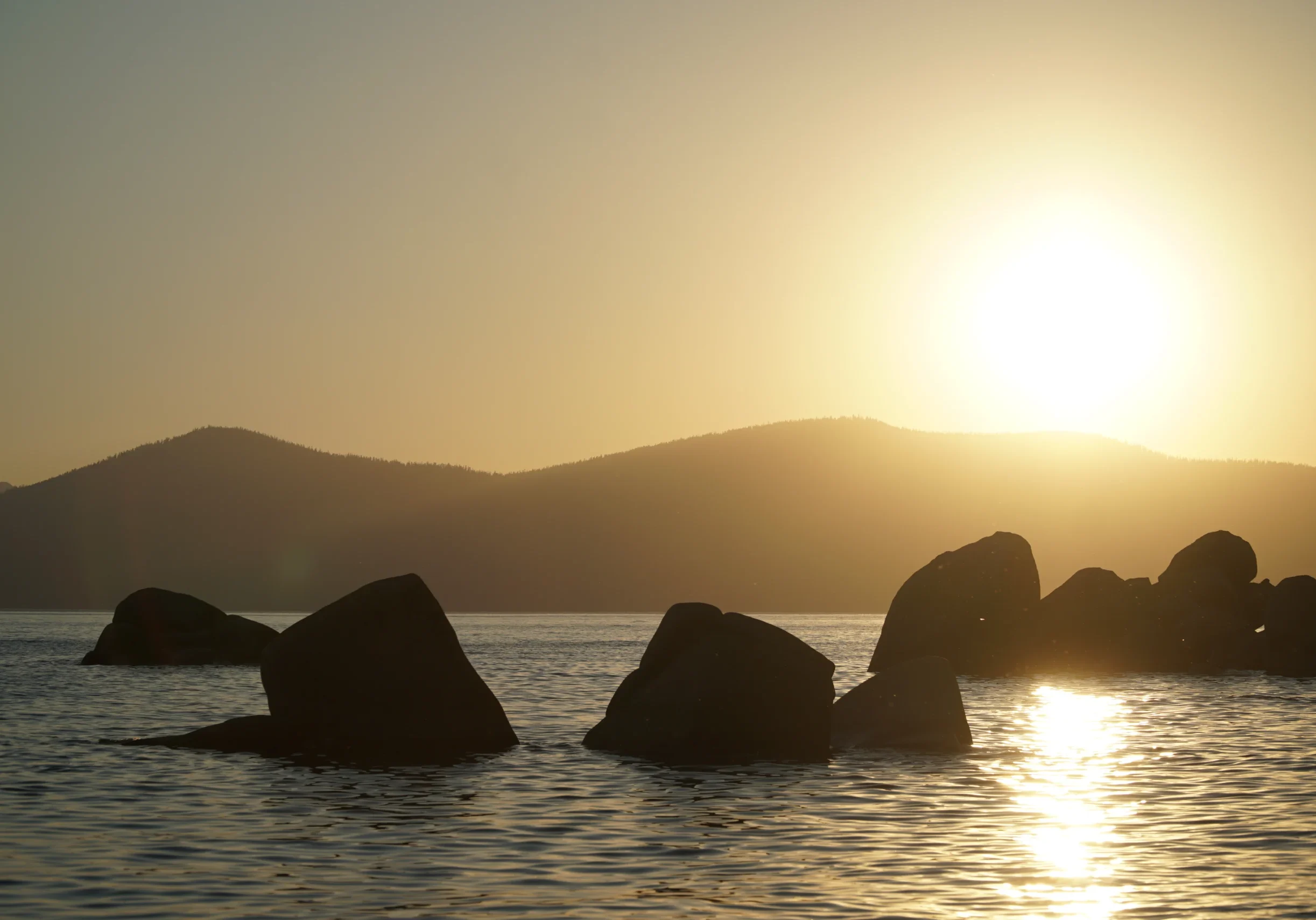 Large boulders exposed in a lake with a sunrise and mountain view in the background